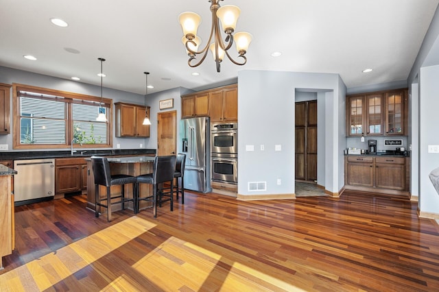 kitchen with dark wood-type flooring, a notable chandelier, decorative light fixtures, a breakfast bar, and appliances with stainless steel finishes