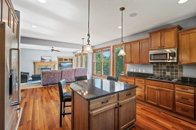 kitchen featuring dark wood-type flooring, appliances with stainless steel finishes, decorative light fixtures, a kitchen island, and a kitchen bar