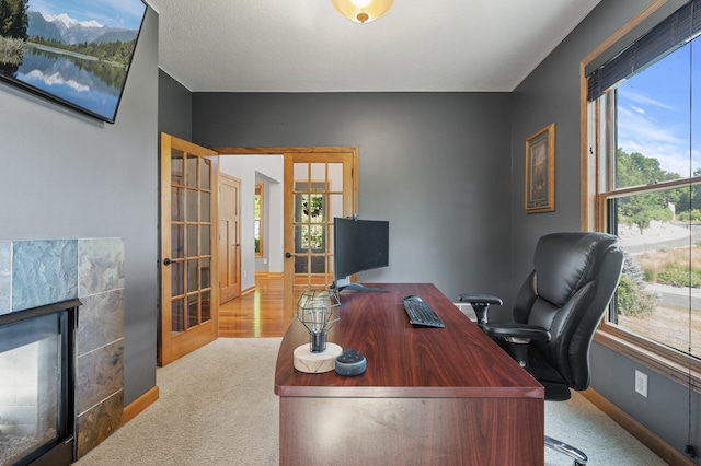 carpeted home office featuring a tiled fireplace, a textured ceiling, and french doors