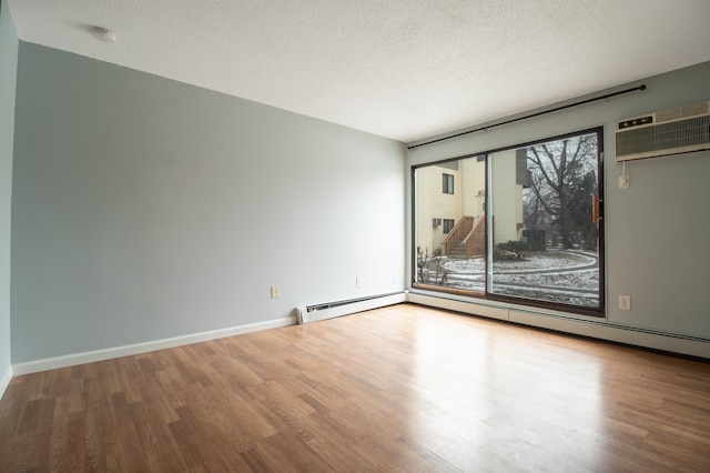 empty room featuring a wall unit AC, hardwood / wood-style floors, a textured ceiling, and baseboard heating