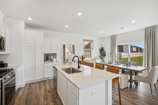 kitchen with a center island with sink, sink, light stone countertops, appliances with stainless steel finishes, and white cabinetry