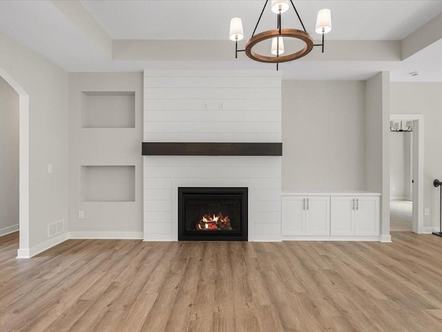 unfurnished living room featuring a notable chandelier, visible vents, light wood-style flooring, a large fireplace, and baseboards