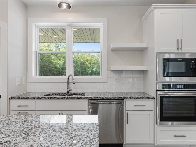 kitchen with stainless steel appliances, a sink, white cabinets, decorative backsplash, and light stone countertops