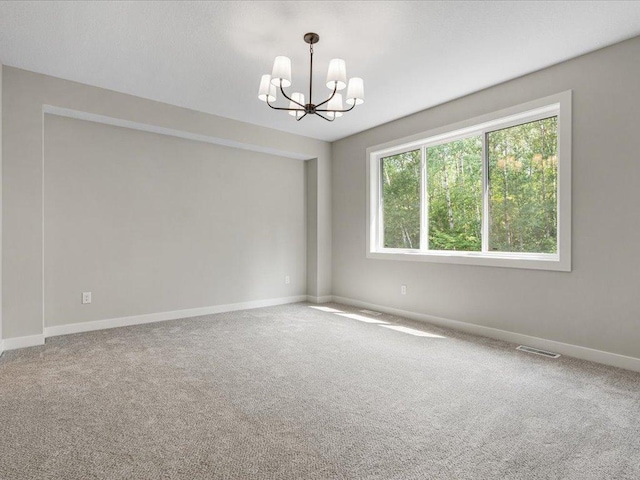 spare room with carpet floors, visible vents, baseboards, and an inviting chandelier