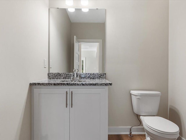 half bathroom with toilet, baseboards, wood finished floors, and vanity