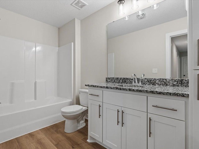 bathroom with a textured ceiling, toilet, wood finished floors, vanity, and visible vents