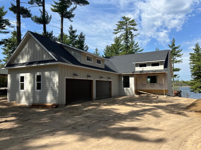 view of front facade featuring board and batten siding, dirt driveway, a garage, a water view, and covered porch