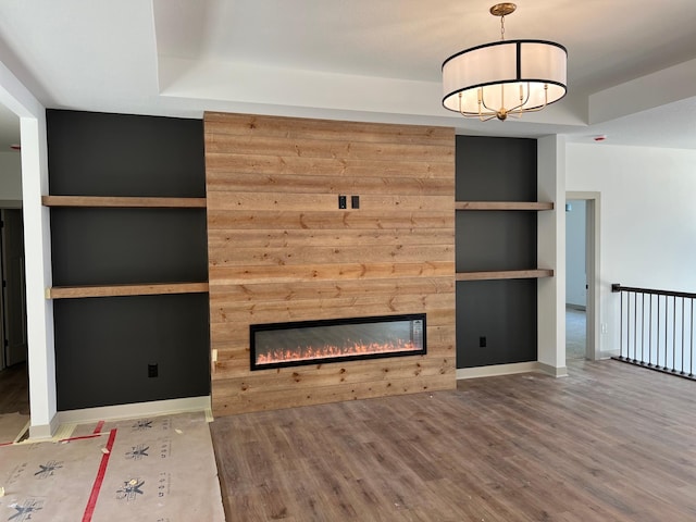 unfurnished living room with wood finished floors, a glass covered fireplace, a raised ceiling, and a chandelier