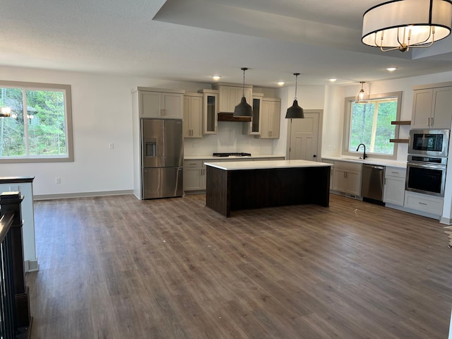 kitchen featuring stainless steel appliances, dark wood finished floors, light countertops, baseboards, and a center island