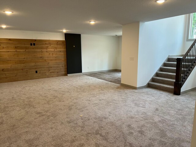 below grade area featuring carpet floors, stairway, wood walls, recessed lighting, and baseboards