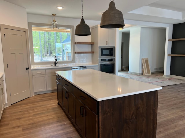 kitchen with a sink, appliances with stainless steel finishes, open shelves, light countertops, and light wood-style flooring