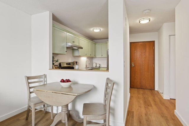 kitchen with kitchen peninsula, sink, light hardwood / wood-style flooring, stainless steel stove, and green cabinets