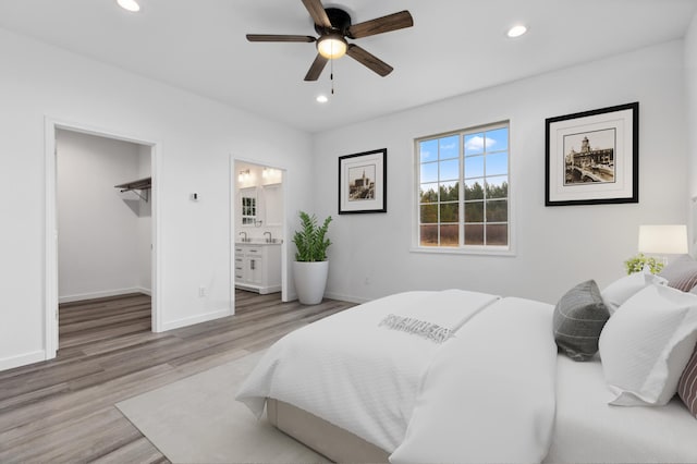 bedroom featuring ensuite bathroom, a walk in closet, light hardwood / wood-style flooring, ceiling fan, and a closet