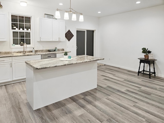 kitchen featuring light stone countertops, sink, hanging light fixtures, a kitchen island, and white cabinets