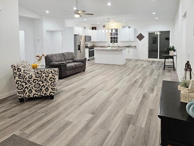 living room with ceiling fan, sink, light hardwood / wood-style floors, and vaulted ceiling