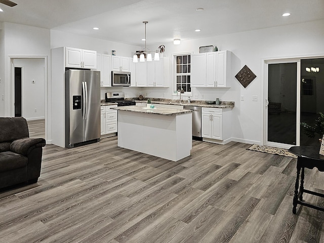 kitchen featuring a center island, white cabinets, light stone countertops, appliances with stainless steel finishes, and decorative light fixtures