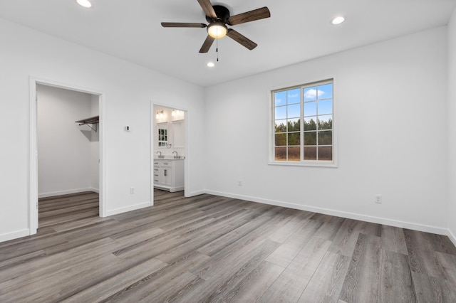 unfurnished bedroom with ceiling fan, a spacious closet, connected bathroom, wood-type flooring, and a closet