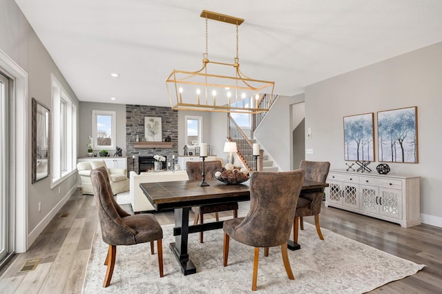 dining area with light hardwood / wood-style floors, a stone fireplace, and an inviting chandelier