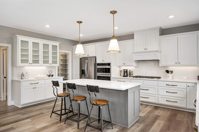 kitchen with hardwood / wood-style flooring, white cabinets, stainless steel appliances, and hanging light fixtures