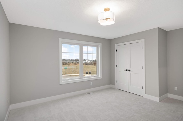 unfurnished bedroom with light colored carpet and a closet