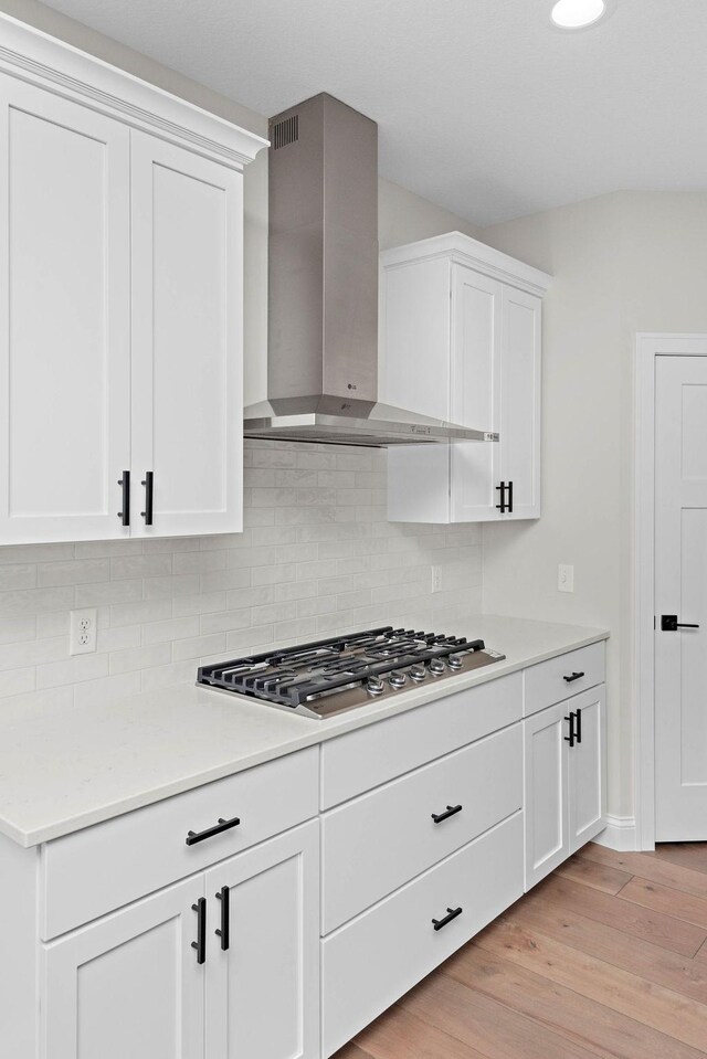 kitchen featuring backsplash, wall chimney range hood, light hardwood / wood-style floors, white cabinetry, and stainless steel gas cooktop