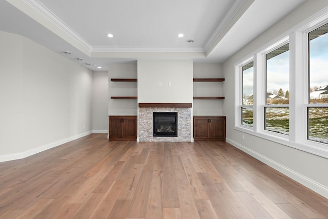 unfurnished living room featuring a tray ceiling, a stone fireplace, light hardwood / wood-style floors, and ornamental molding