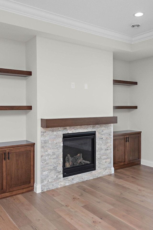 interior details with a stone fireplace, wood-type flooring, and ornamental molding