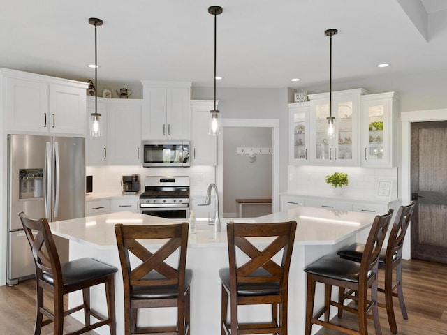 kitchen with an island with sink, appliances with stainless steel finishes, decorative backsplash, and white cabinetry