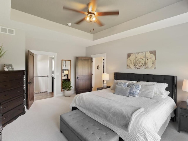 carpeted bedroom with a raised ceiling and ceiling fan