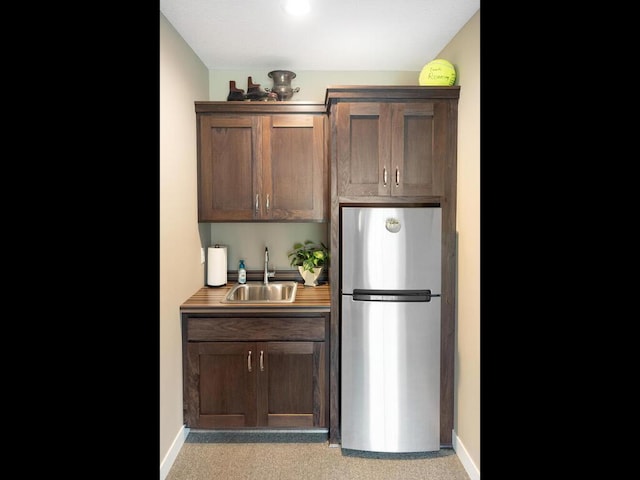 bar featuring light colored carpet, stainless steel fridge, dark brown cabinets, and sink