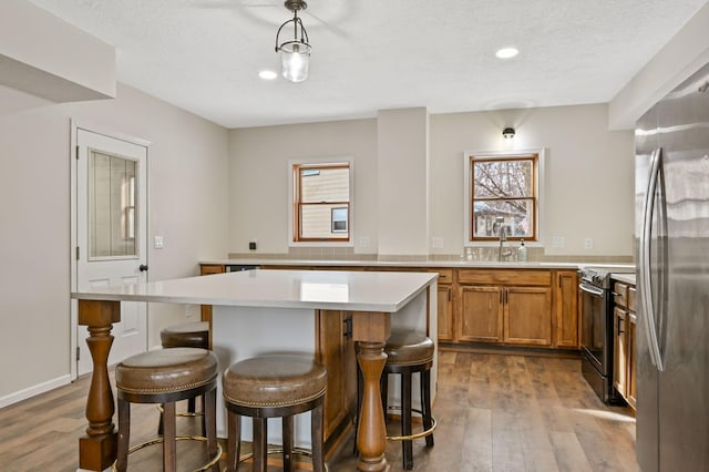 kitchen featuring a kitchen island, electric range oven, stainless steel fridge, hanging light fixtures, and hardwood / wood-style flooring