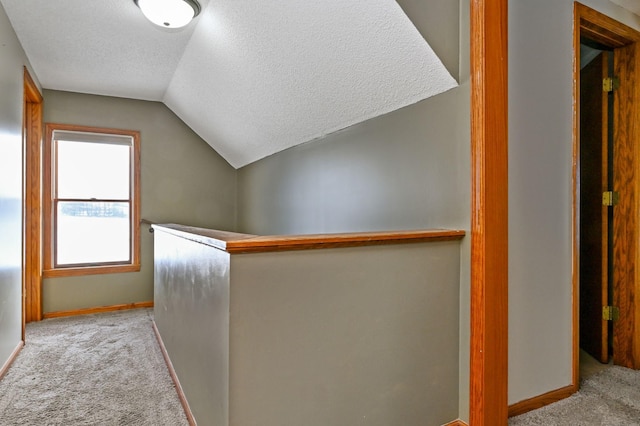 hallway with light carpet, lofted ceiling, and a textured ceiling