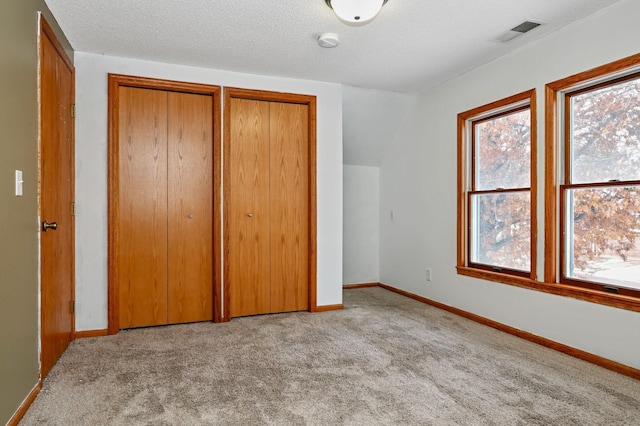 unfurnished bedroom featuring a textured ceiling, multiple closets, and light colored carpet