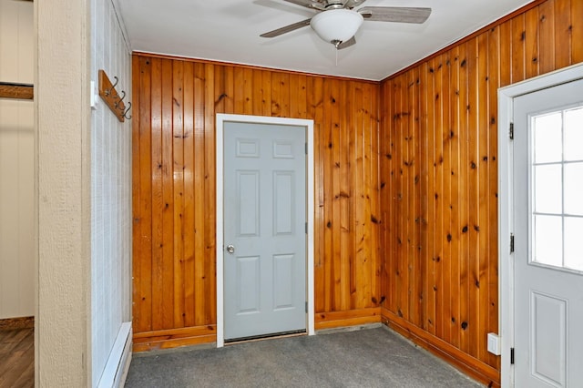 entryway featuring ceiling fan, dark colored carpet, wood walls, and a healthy amount of sunlight