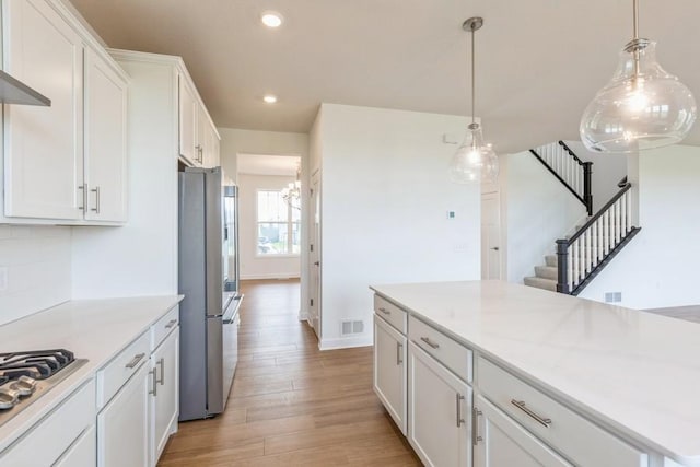 kitchen with appliances with stainless steel finishes, decorative light fixtures, light hardwood / wood-style flooring, a notable chandelier, and white cabinetry