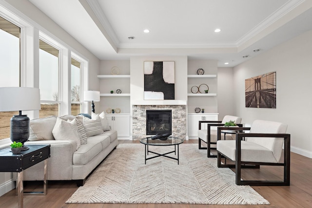 living room with built in features, hardwood / wood-style flooring, a stone fireplace, and a tray ceiling