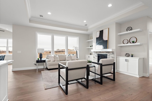 living room featuring a raised ceiling, built in shelves, dark hardwood / wood-style flooring, and a stone fireplace