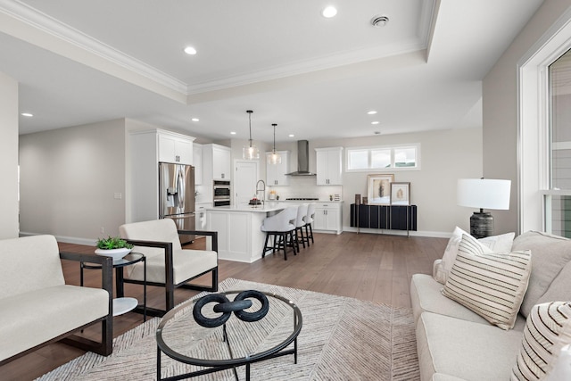 living room with sink, a raised ceiling, wood-type flooring, and ornamental molding