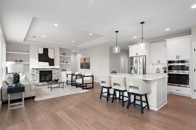 kitchen with appliances with stainless steel finishes, a tray ceiling, a large island with sink, decorative light fixtures, and white cabinets