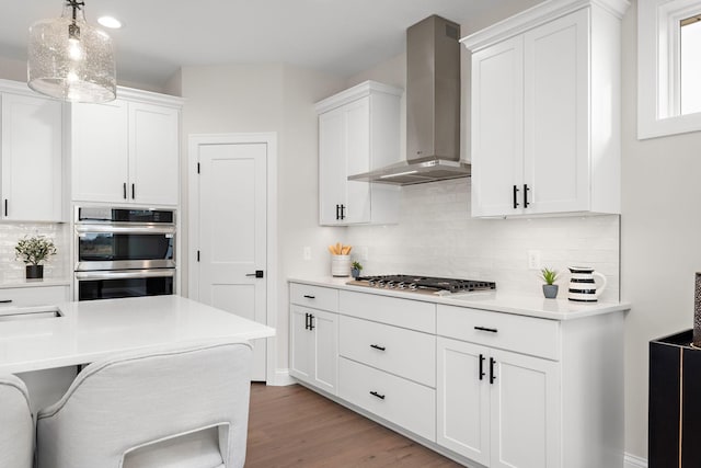 kitchen with wall chimney exhaust hood, stainless steel appliances, decorative light fixtures, white cabinets, and a breakfast bar area