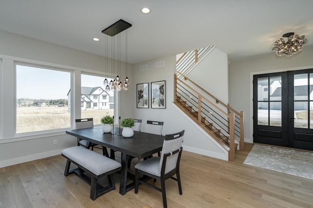 dining space featuring light wood finished floors, baseboards, a chandelier, stairway, and french doors