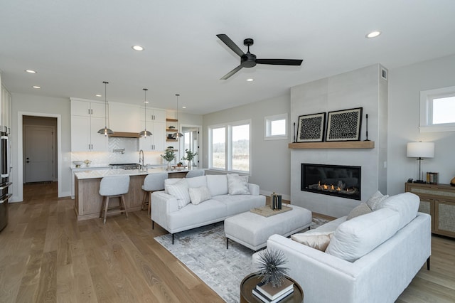 living area with baseboards, ceiling fan, light wood-type flooring, recessed lighting, and a fireplace