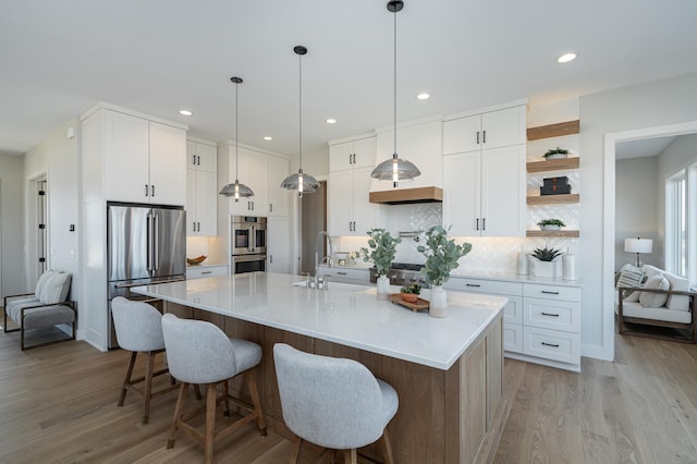 kitchen with a sink, white cabinetry, light wood-style floors, appliances with stainless steel finishes, and decorative backsplash