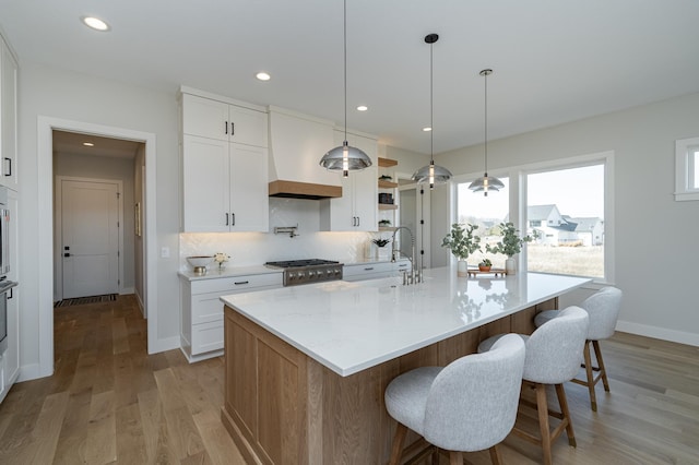 kitchen with light wood-style flooring, a sink, custom range hood, range, and backsplash