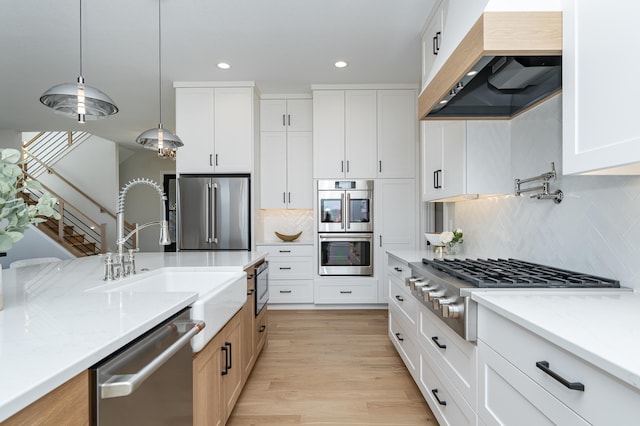 kitchen featuring light stone countertops, light wood finished floors, a sink, stainless steel appliances, and wall chimney exhaust hood