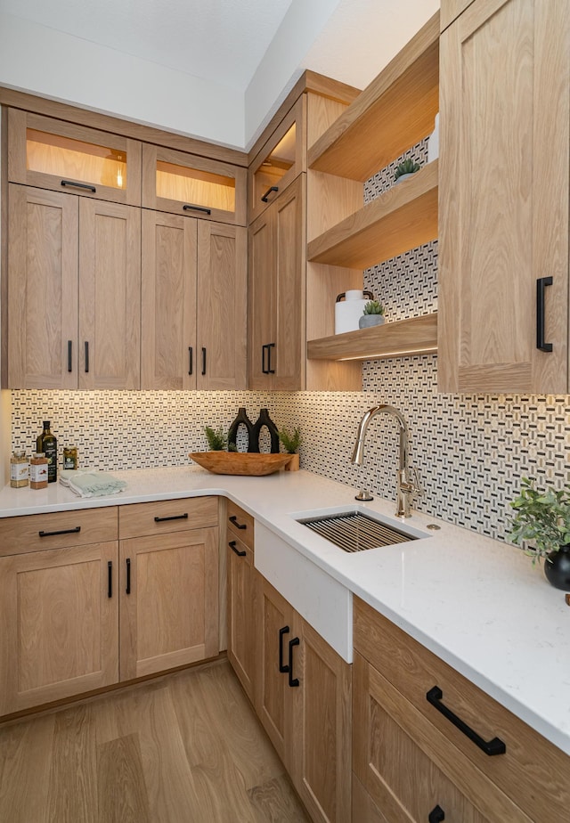 kitchen featuring a sink, glass insert cabinets, decorative backsplash, light wood-style floors, and open shelves