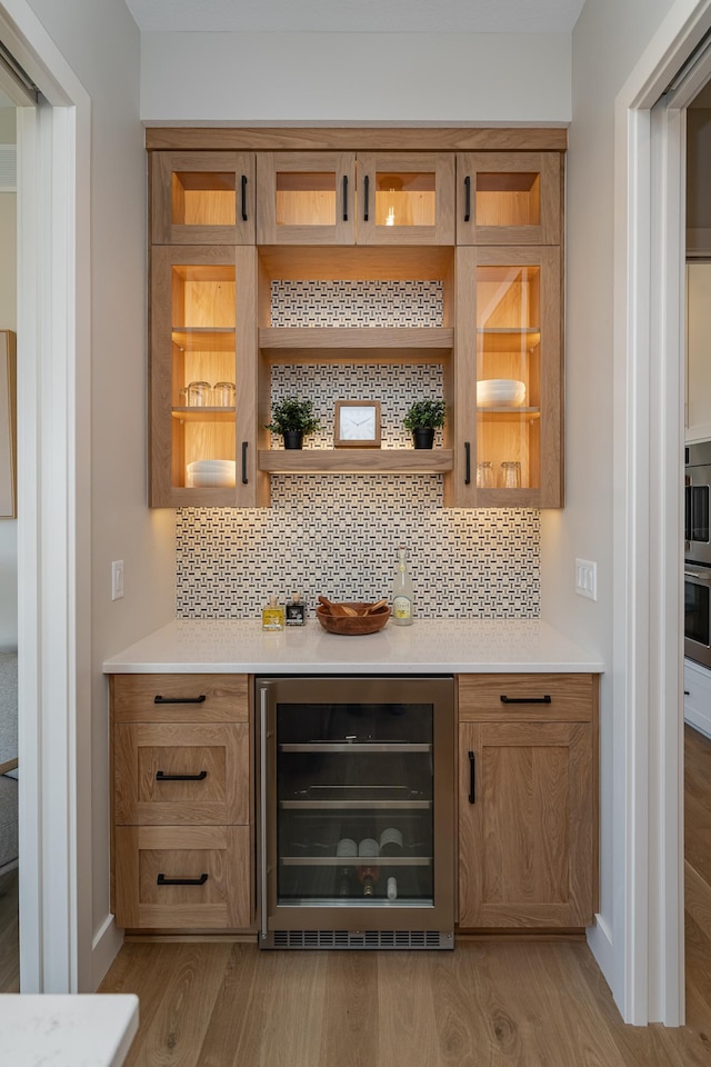 bar featuring light wood-style flooring, wine cooler, backsplash, and a dry bar