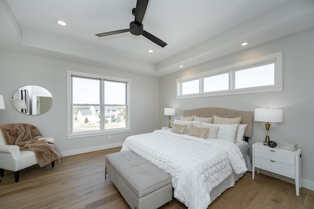 bedroom with a tray ceiling, recessed lighting, light wood-style floors, and baseboards