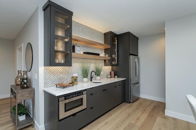 kitchen featuring tasteful backsplash, baseboards, light countertops, light wood-type flooring, and a sink