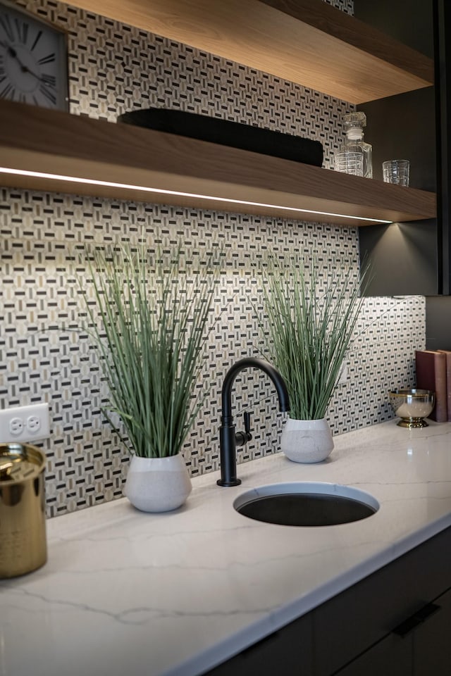 room details featuring open shelves, light stone counters, tasteful backsplash, and a sink